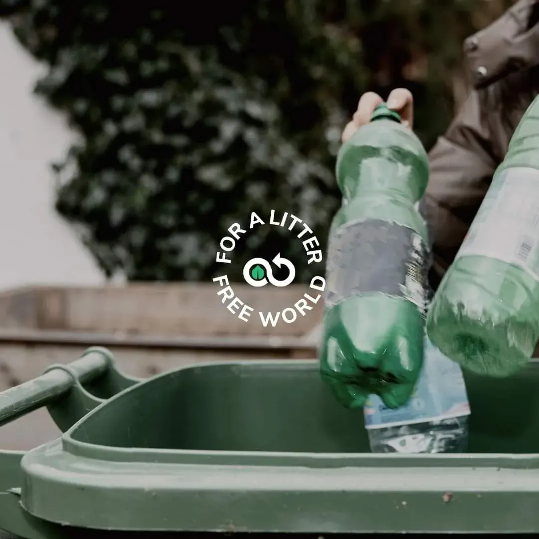 Person placing a plastic bottle into a recycling bin outdoors, supporting a local bottle collection effort.