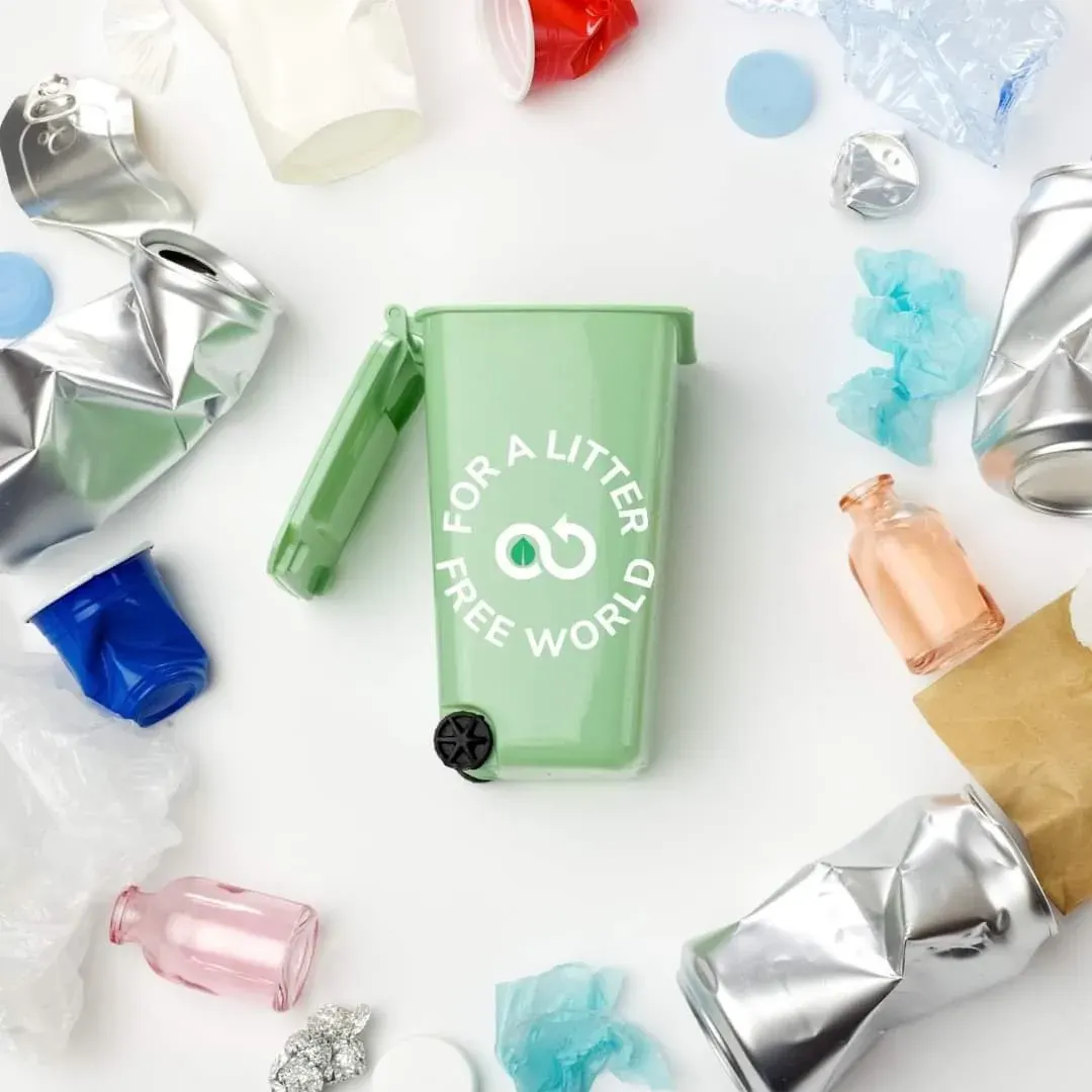 Green compact bin with 'FOR A LITTER FREE WORLD' among plastic bottles, cans, lids and wrappers, relevant to plastic bottle collection in the UAE. Green compact bin with 'FOR A LITTER FREE WORLD' among plastic bottles, cans, lids and wrappers, relevant to plastic bottle collection in the UAE.