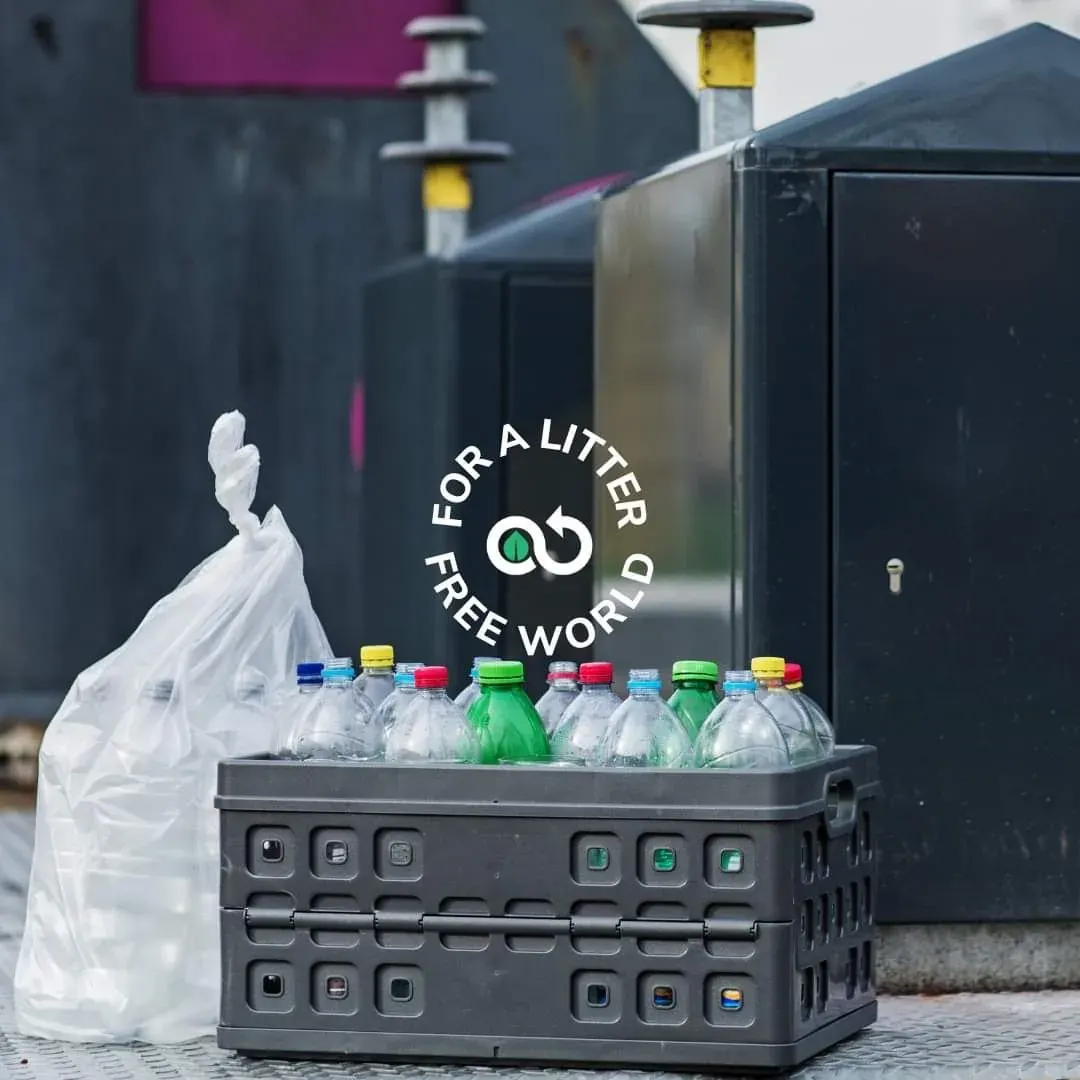 Cardboard crate of empty plastic bottles beside a garbage bin, reflecting local recycling and anti-litter action Cardboard crate of empty plastic bottles beside a garbage bin, reflecting local recycling and anti-litter action
